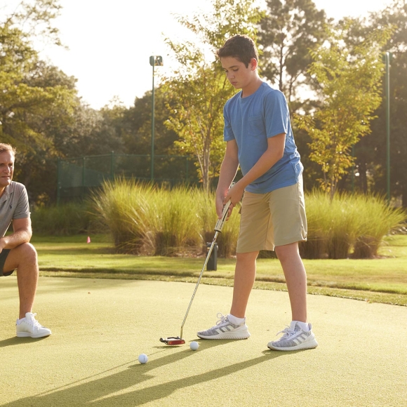 Father and son on putting green and the son is about to take his shot