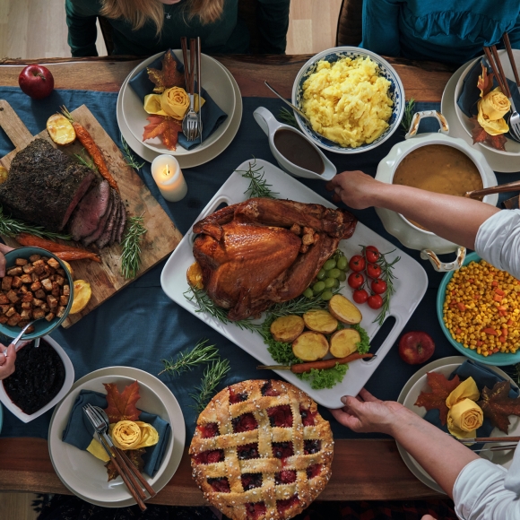 Thanksgiving feast spread out on a table with a family sitting around passing food