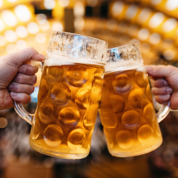 Two people cheering two beers in front an arch of lights