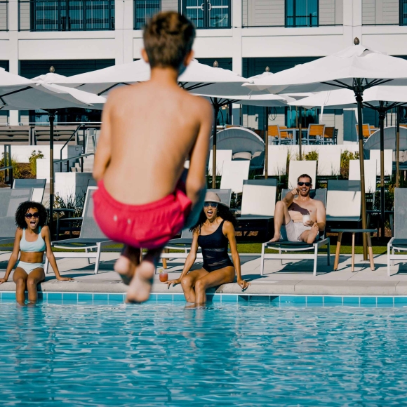 A boy doing a cannon ball into the pool while his family watches