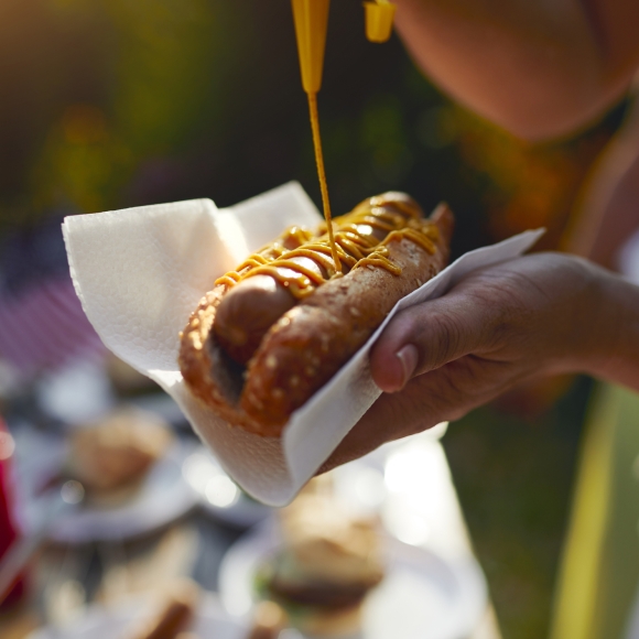 Close up of mustard being drizzled on a hot dog