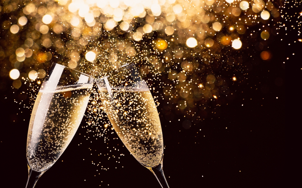 Two glasses of champagne toasting in the nigh with lights bokeh, glitter and sparks on the background