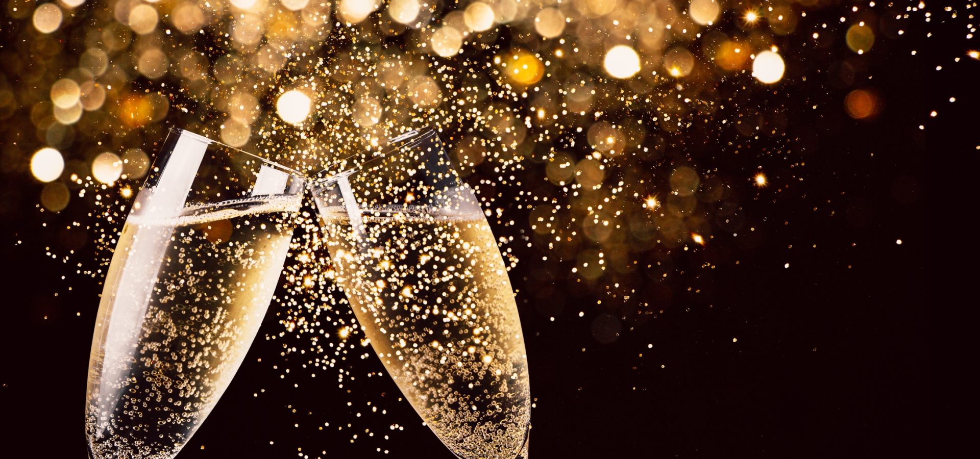 Two glasses of champagne toasting in the nigh with lights bokeh, glitter and sparks on the background